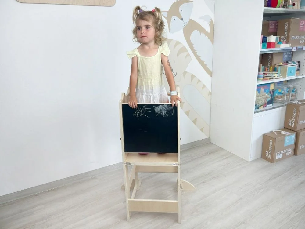 Mergaitė stovi mokymosi bokšte už kreidinės lentos