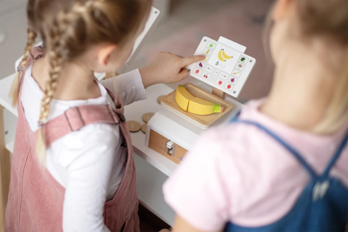 Mergaitės rodo vaisių kortelę prie svarstyklių ekrano